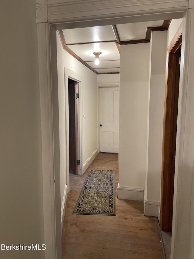 hallway featuring baseboards, wood finished floors, and crown molding