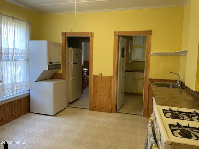 kitchen with stacked washing maching and dryer, wooden walls, sink, crown molding, and white appliances