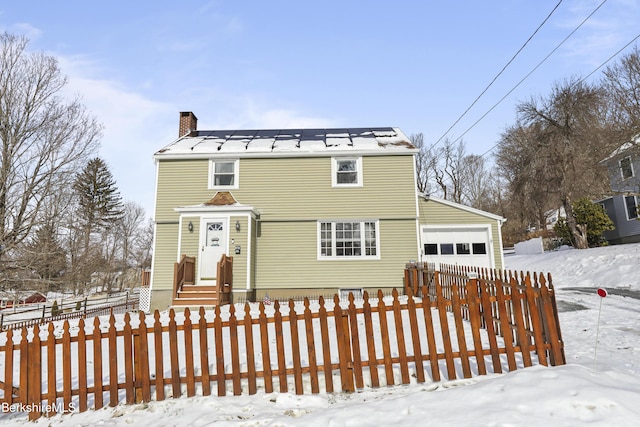 view of front of house featuring a garage, a fenced front yard, a chimney, metal roof, and a standing seam roof