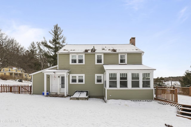 snow covered back of property featuring a chimney, fence, and a wooden deck