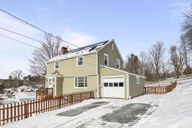 view of snowy property with a garage, fence, and a chimney