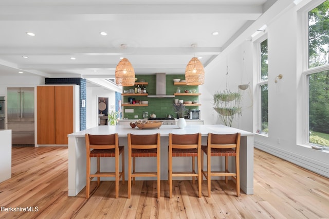 kitchen featuring built in refrigerator, beam ceiling, wall chimney exhaust hood, and light wood-style floors