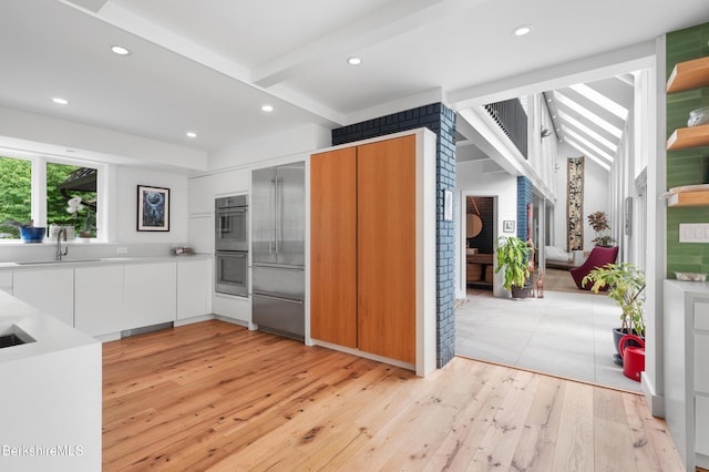 kitchen with white cabinetry, modern cabinets, light wood finished floors, double oven, and a sink
