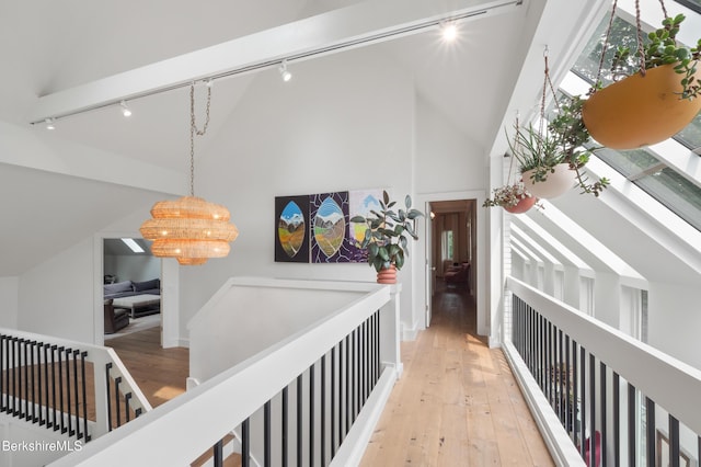 hallway with light wood finished floors, rail lighting, and an inviting chandelier