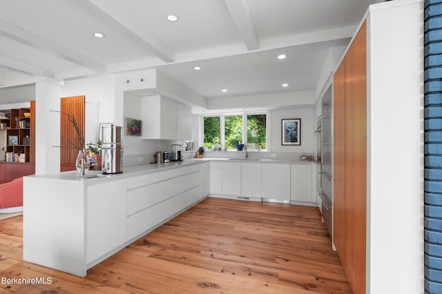 kitchen featuring light wood finished floors, a peninsula, beamed ceiling, and modern cabinets
