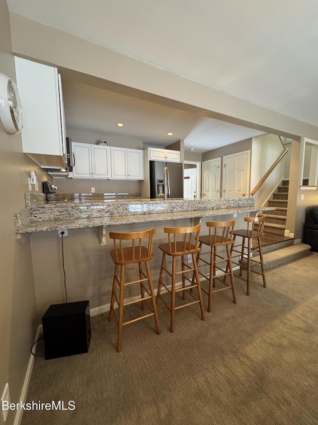 kitchen featuring a kitchen bar, stainless steel fridge, white cabinets, and kitchen peninsula