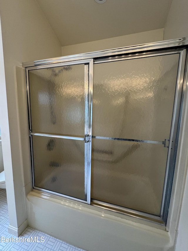 bathroom with tile patterned floors, toilet, and bath / shower combo with glass door