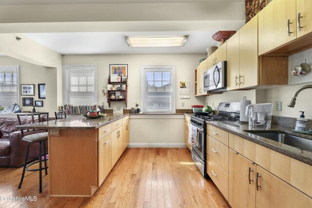 kitchen featuring a sink, dark stone countertops, appliances with stainless steel finishes, a breakfast bar area, and a peninsula