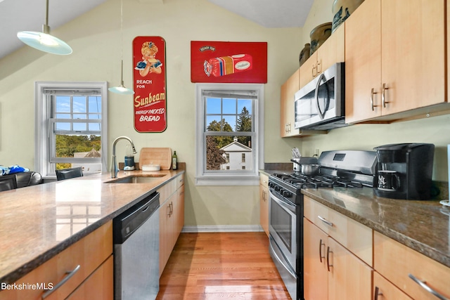 kitchen with light wood finished floors, stainless steel appliances, dark stone counters, and a sink