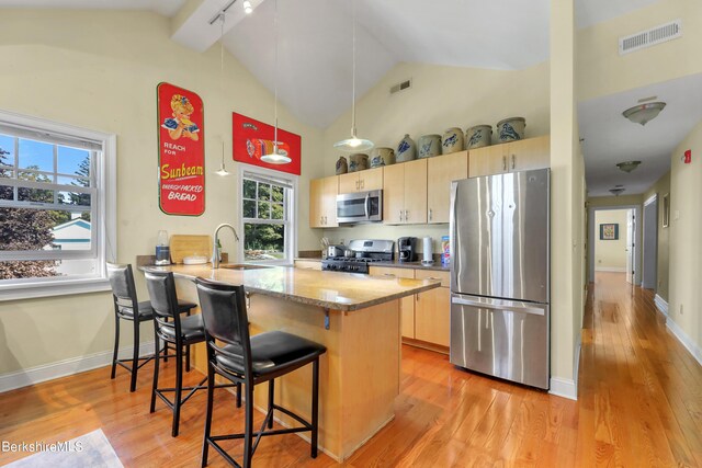 kitchen with visible vents, a peninsula, a sink, light brown cabinetry, and appliances with stainless steel finishes