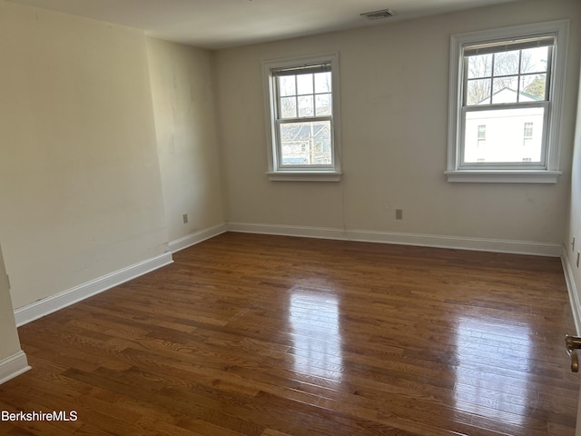 unfurnished room featuring baseboards, visible vents, and dark wood finished floors