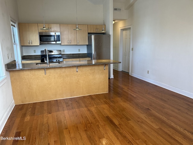 kitchen with a breakfast bar, stainless steel appliances, a peninsula, dark wood-style flooring, and visible vents