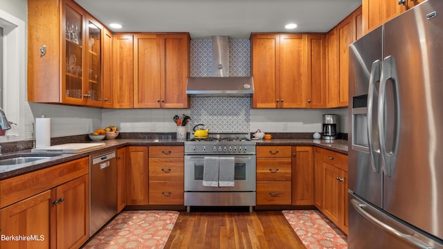 kitchen featuring decorative backsplash, wall chimney exhaust hood, stainless steel appliances, sink, and dark stone countertops