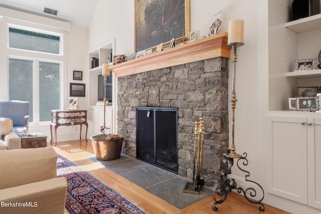 living room featuring built in features, hardwood / wood-style flooring, a stone fireplace, and lofted ceiling