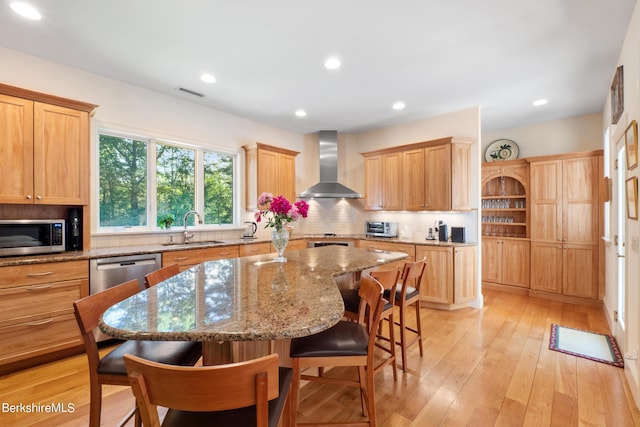 kitchen with a center island, sink, stainless steel appliances, wall chimney range hood, and a kitchen bar