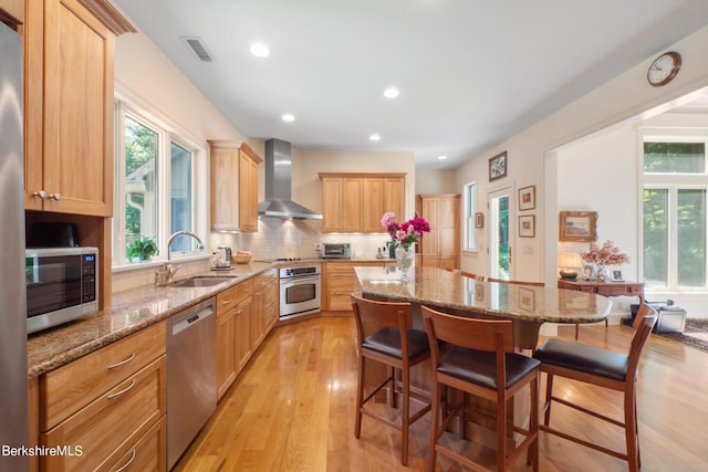 kitchen featuring appliances with stainless steel finishes, a breakfast bar, sink, wall chimney range hood, and a kitchen island