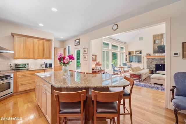 kitchen with stainless steel oven, light brown cabinetry, tasteful backsplash, a kitchen island, and a breakfast bar area