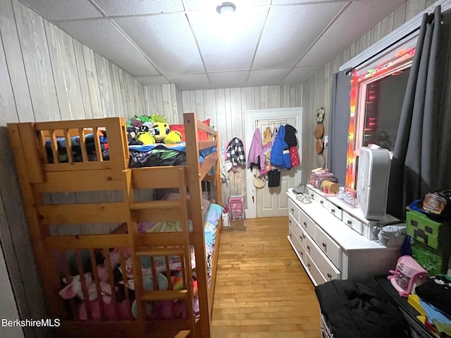 bedroom with wood walls, a drop ceiling, and light wood-type flooring