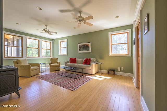 living room featuring baseboards, a wood stove, a ceiling fan, and light wood-type flooring