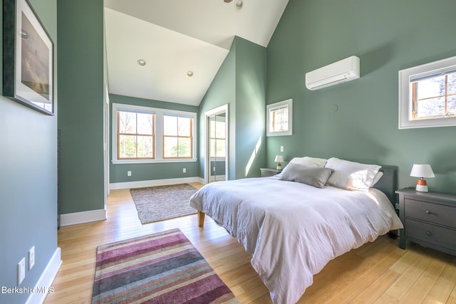 bedroom featuring high vaulted ceiling, baseboards, a wall mounted AC, and light wood finished floors
