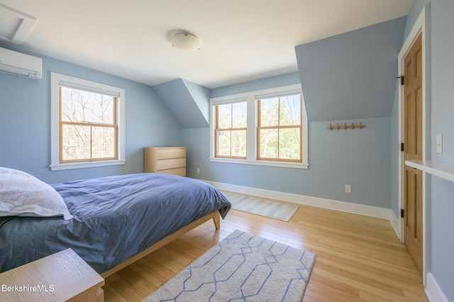 bedroom featuring light wood-style floors, baseboards, a wall unit AC, and multiple windows