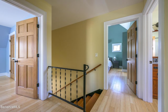 hallway with light wood-style floors, baseboards, and an upstairs landing