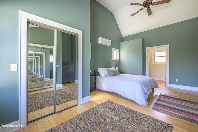 bedroom with ceiling fan, a wall mounted AC, wood finished floors, high vaulted ceiling, and baseboards