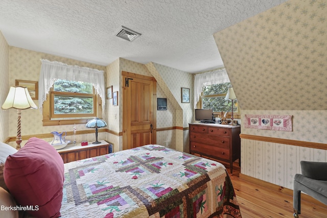 135 E St, Lee, MA 01238 - bedroom featuring wallpapered walls, wood-type flooring, and a textured ceiling