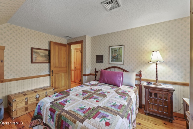 135 E St, Lee, MA 01238 - bedroom featuring light wood-style floors, a wainscoted wall, a textured ceiling, and wallpapered walls