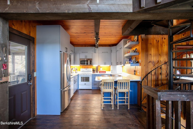 kitchen with a breakfast bar, white cabinets, dark hardwood / wood-style floors, appliances with stainless steel finishes, and wood ceiling