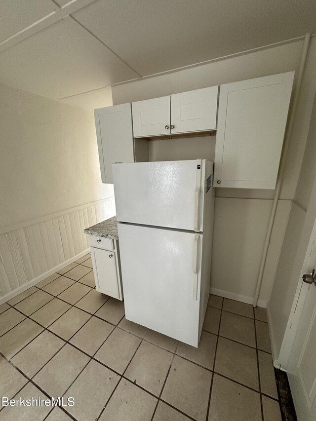 kitchen with white refrigerator, light stone countertops, white cabinetry, and light tile patterned floors