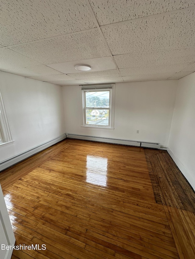 unfurnished room featuring hardwood / wood-style flooring, baseboard heating, and a drop ceiling