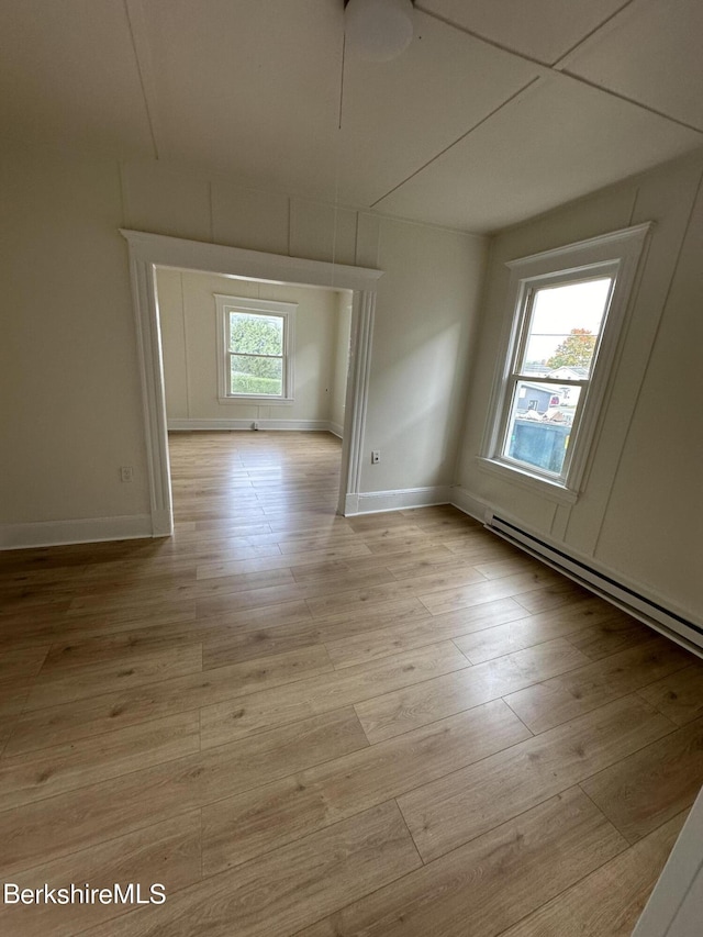 empty room featuring light wood-type flooring, a wealth of natural light, and a baseboard radiator