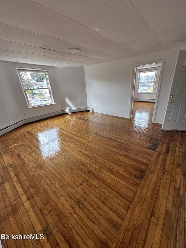 empty room with hardwood / wood-style floors, a drop ceiling, and a baseboard heating unit