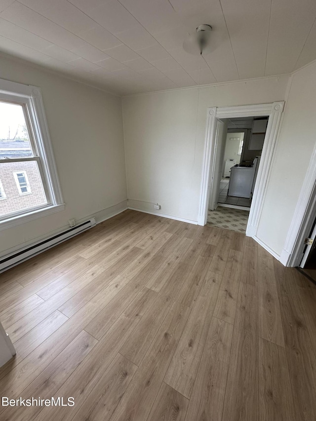 spare room featuring baseboard heating and light hardwood / wood-style flooring