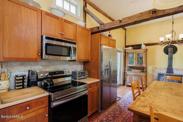 kitchen with a wood stove, an inviting chandelier, appliances with stainless steel finishes, beamed ceiling, and decorative light fixtures