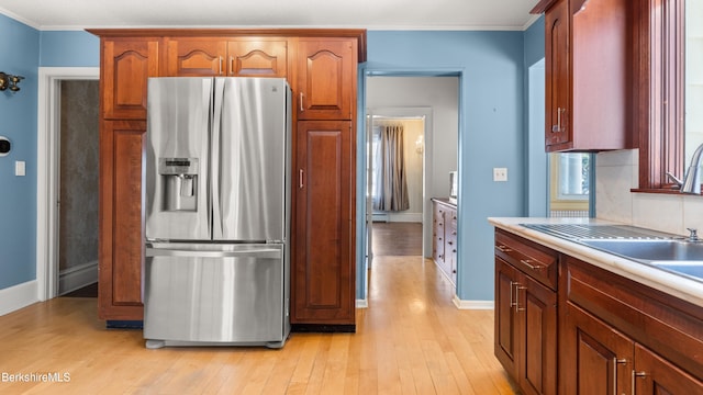 kitchen with light wood-type flooring, a sink, stainless steel fridge, crown molding, and baseboards