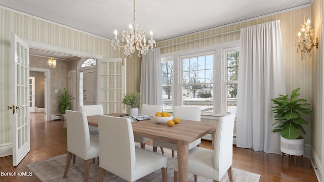 dining area with wallpapered walls, a baseboard heating unit, wood finished floors, a notable chandelier, and a textured ceiling