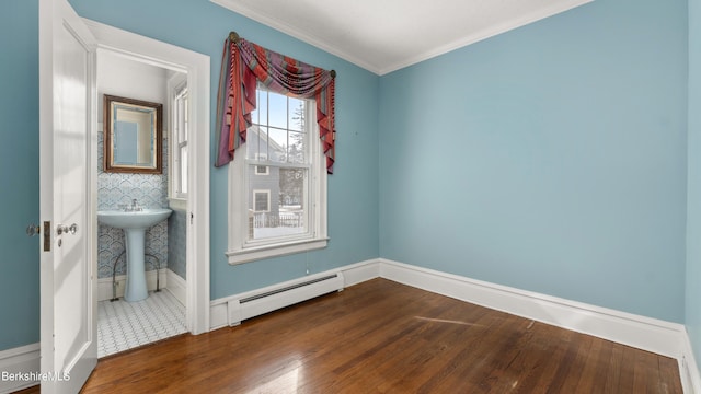 empty room with a baseboard heating unit, wood finished floors, baseboards, and ornamental molding