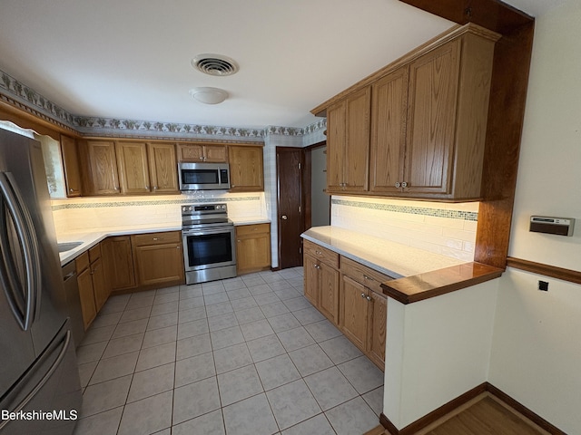 184 Mcintosh Dr, Pittsfield, MA 01201 - kitchen featuring appliances with stainless steel finishes, decorative backsplash, brown cabinets, and light tile patterned floors