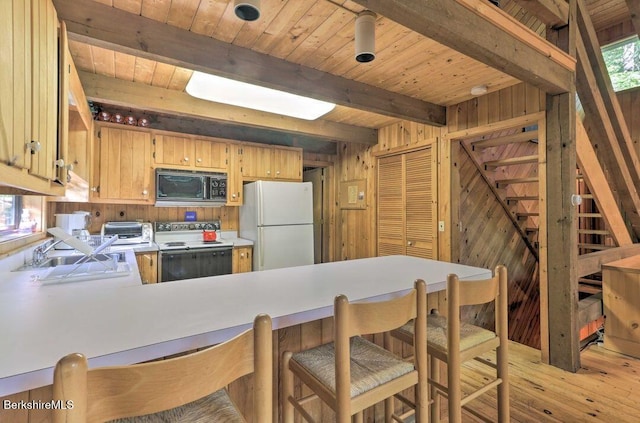kitchen with white appliances, a sink, wooden walls, and a peninsula