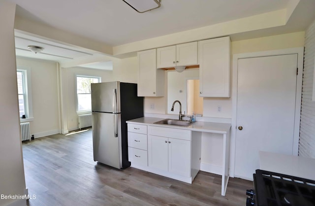 kitchen with white cabinetry, stainless steel refrigerator, radiator, and sink