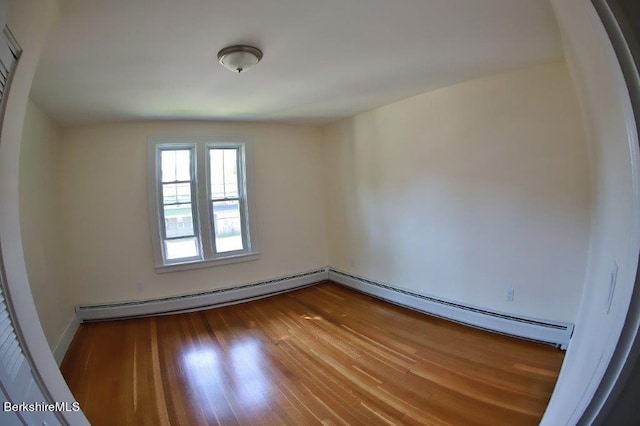 spare room featuring baseboard heating and hardwood / wood-style flooring