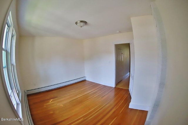 unfurnished room with a wealth of natural light, wood-type flooring, and a baseboard radiator