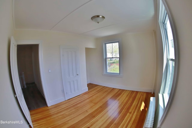 unfurnished bedroom featuring radiator heating unit, light hardwood / wood-style floors, and a closet