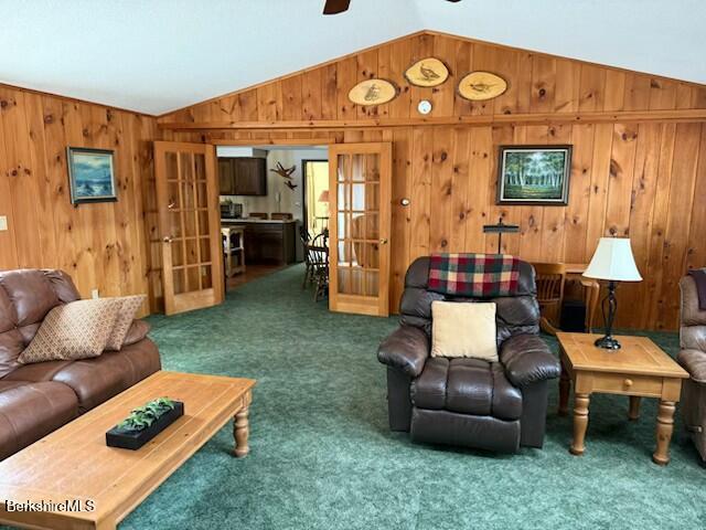 living room with carpet flooring, a wood stove, baseboard heating, lofted ceiling with skylight, and wood walls