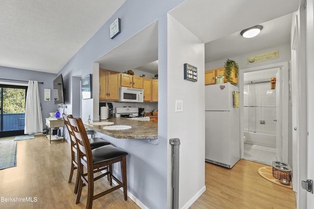 kitchen featuring white appliances, a breakfast bar area, light wood-style flooring, and baseboards