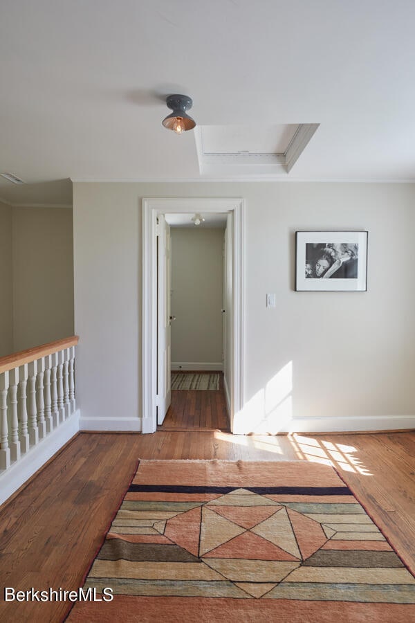 hallway with a tray ceiling, wood-type flooring, and ornamental molding