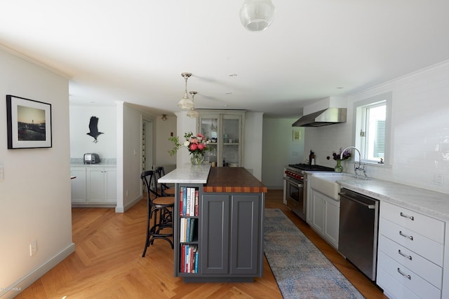 kitchen featuring pendant lighting, wall chimney exhaust hood, appliances with stainless steel finishes, a kitchen island, and butcher block counters