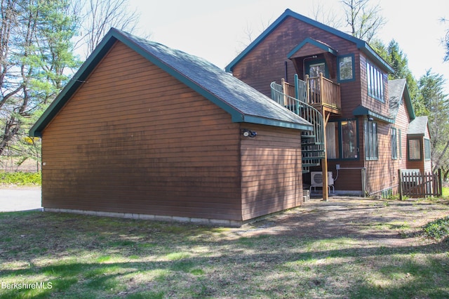 view of side of property featuring a yard, an outdoor structure, a balcony, and roof with shingles